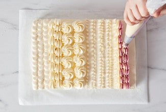 Hands piping designs on a sheet cake