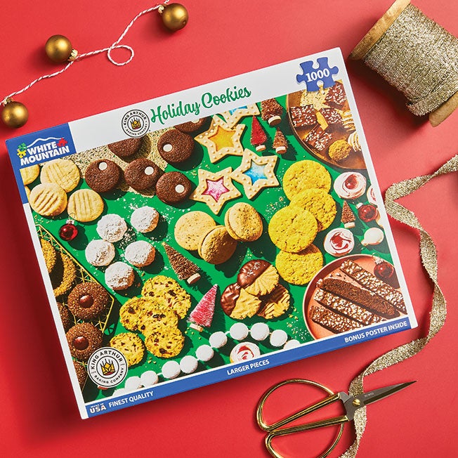 A holiday cookie puzzle on a red table with gold ribbon and decorations spread about.