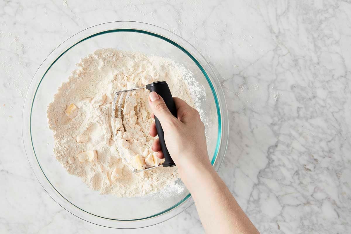 Hand using a pastry cutter to cut butter into a bowl of flour 