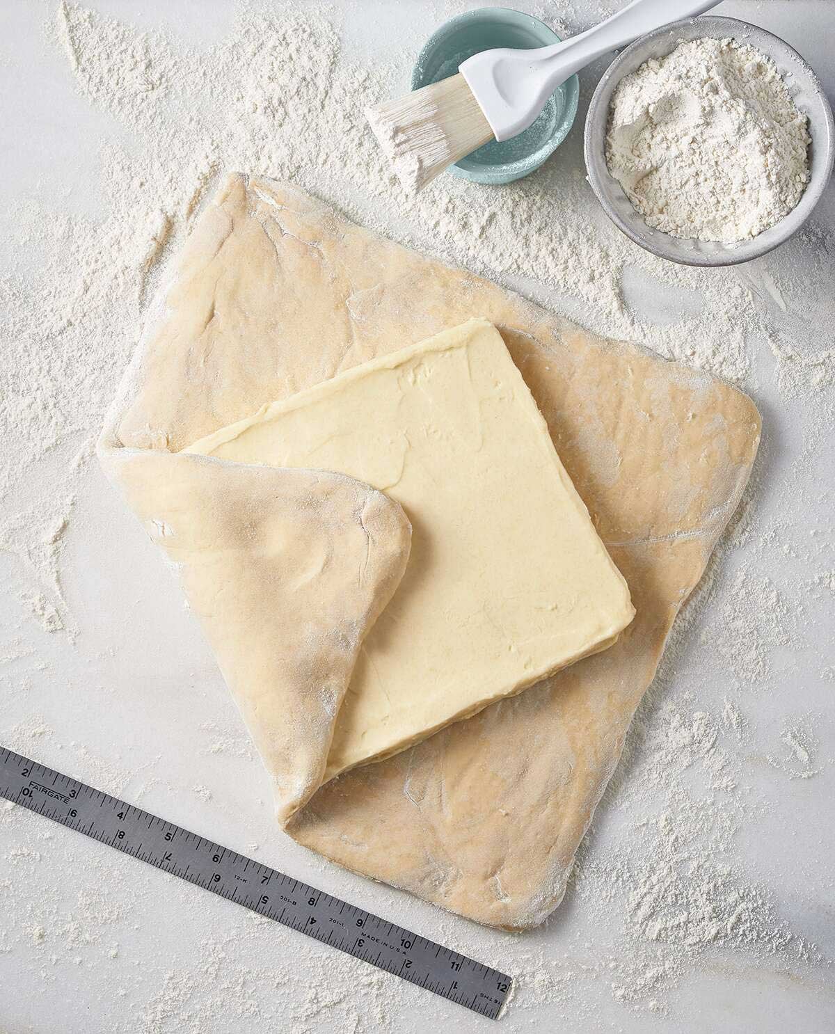 Rolled out pastry dough, with a butter block centered in the middle, ready to be folded up and rolled out