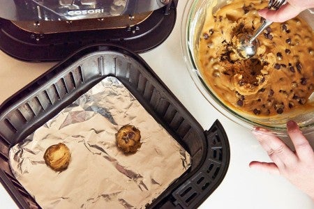 Scooping chocolate chip cookies dough into air fryer basket 