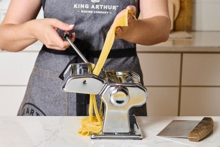 Cranking a pasta maker to cut noodles