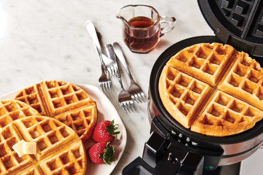 Waffle iron next to plate of waffles