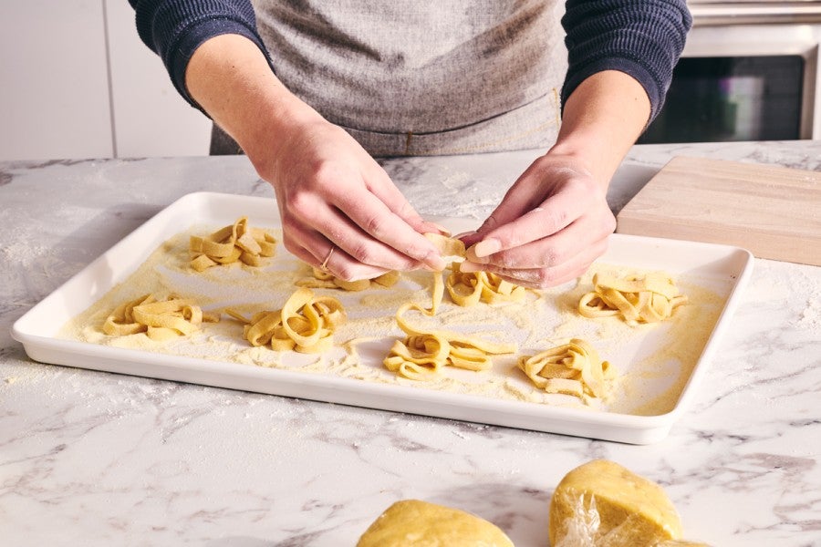 Coiling hand-rolled pasta into nests on baking sheet