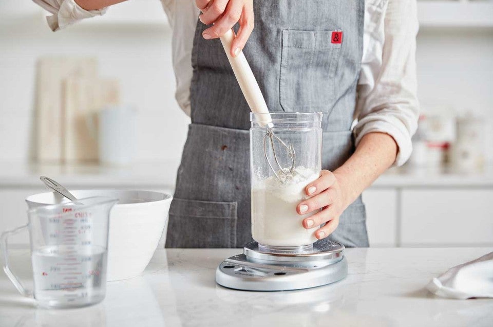 Baker mixing starter with dough whisk