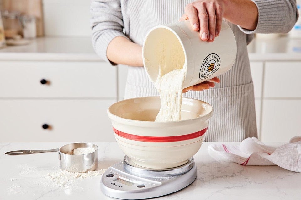 A baker pouring sourdough starter into a bowl to prep it for baking