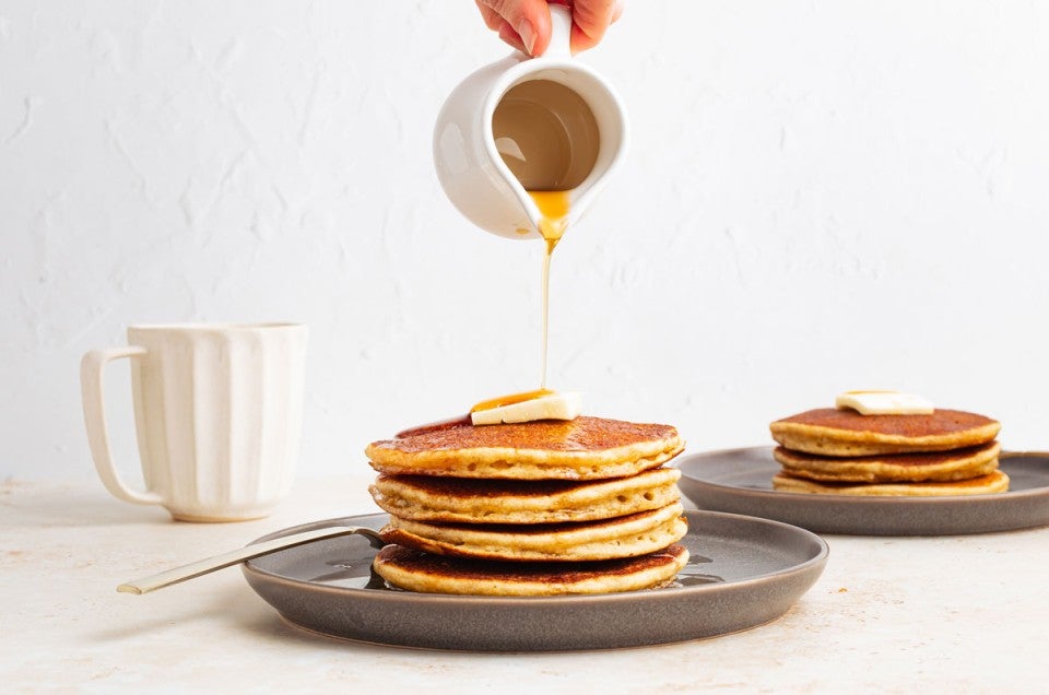 Syrup being poured onto a stack of pancakes