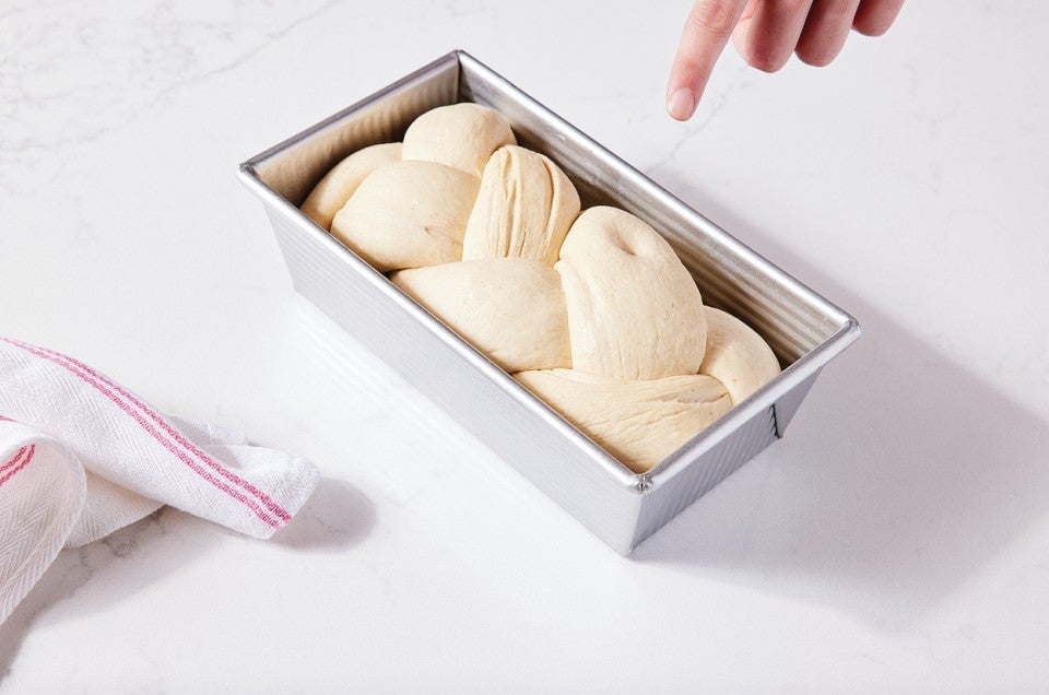 Braided bread dough in loaf pan, with visible indention from poke test