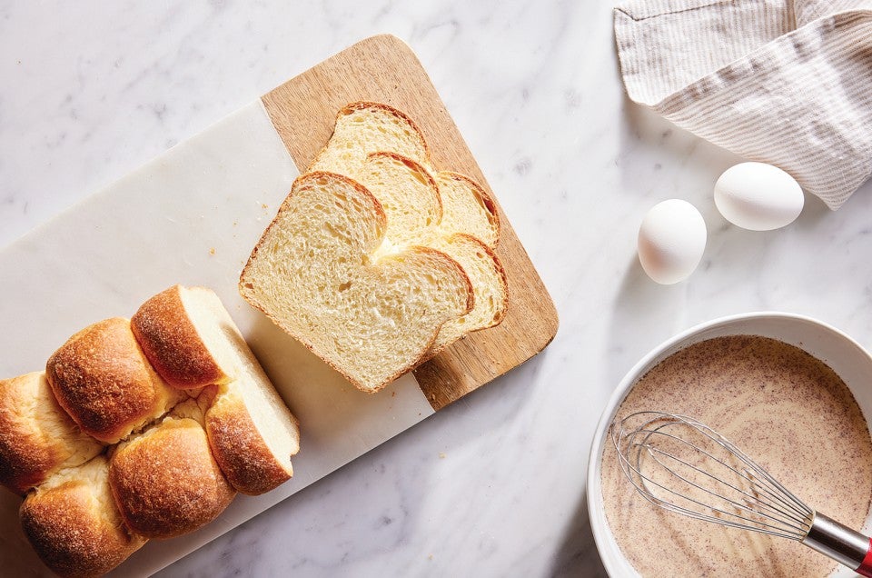 Sliced brioche next to eggs and mixing bowl