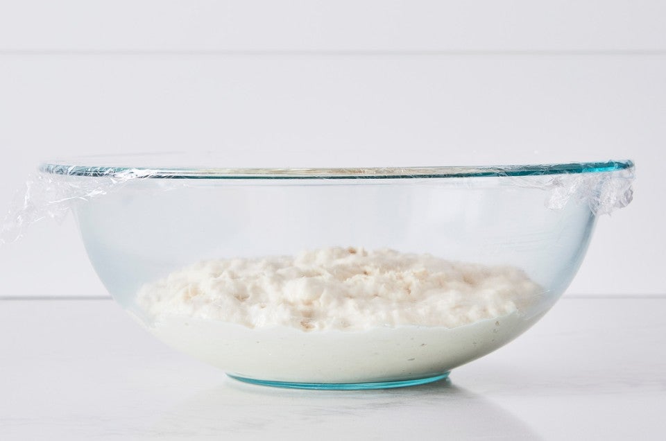 Bread dough in clear glass bowl with plastic wrap covering