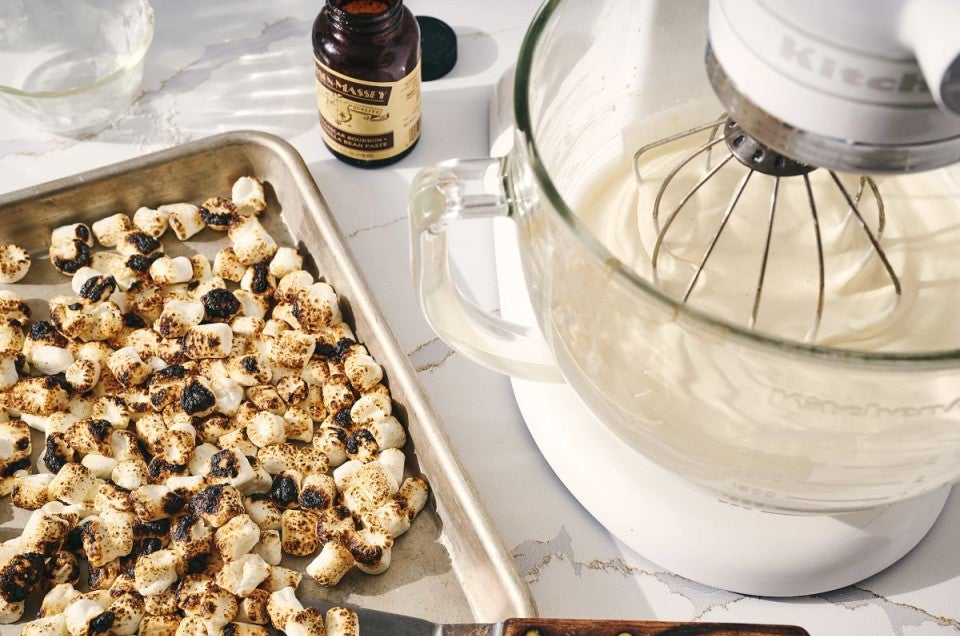 A baking sheet filled with roasted marshmallows next to a stand mixer bowl of whipped cream