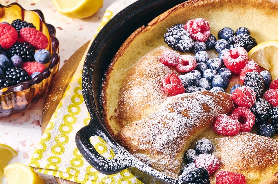 Lemon Puff Pancake with Fresh Berries in a cast iron pan topped with powdered sugar and berries - select to zoom