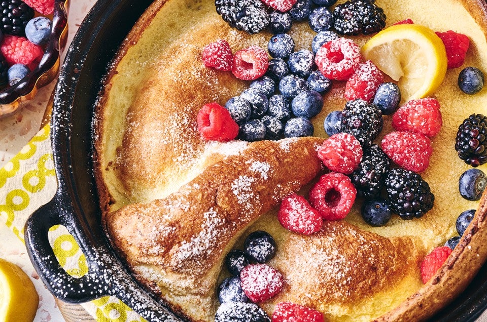 Lemon Puff Pancake with Fresh Berries in a cast iron pan topped with powdered sugar and berries - select to zoom