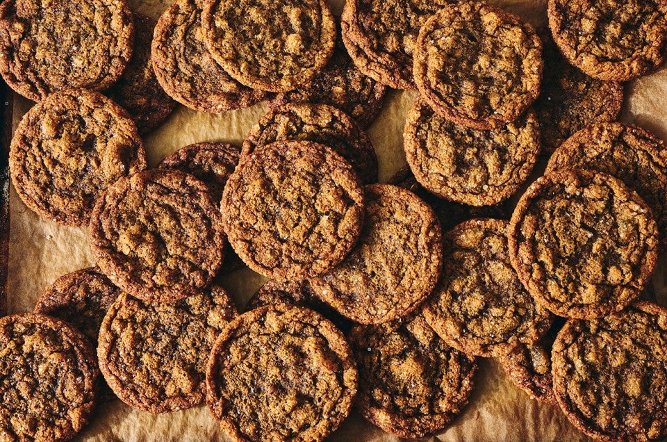 A multitude of Cape Cod Soft Molasses Cookies spread out on dark parchment. - select to zoom