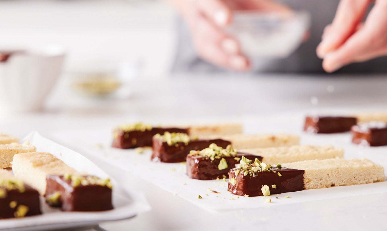 A baker sprinkling salt on top of chocolate-dipped shortbread