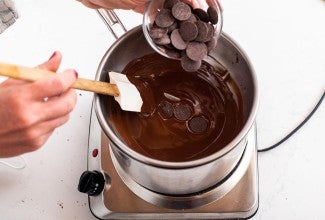 A baker adding seed chocolate to melted chocolate over a double boiler