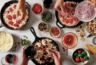 Bakers' hands adding toppings to three different pizzas
