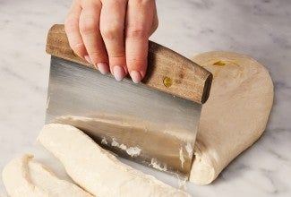 Bench knife being used to cut up wet bread dough