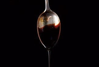 Molasses dripping off a spoon against a black background