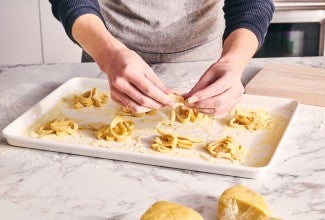 Coiling hand-rolled pasta into nests on baking sheet