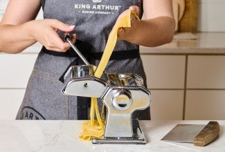 Cranking a pasta maker to cut noodles