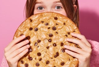 A young girl hiding behind a Chocolate Chip Skillet Cookie