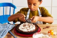 A little boy shaving chocolate onto a pie