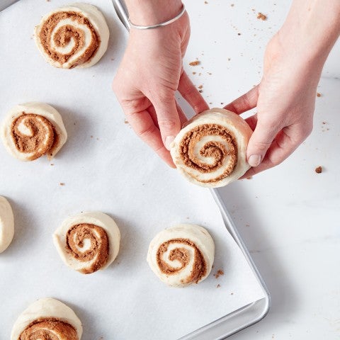 Unbaked cinnamon rolls being placed on baking sheet - select to zoom