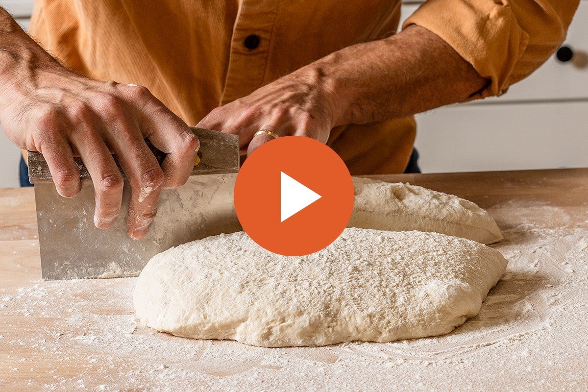 Hands preshaping bread dough, with a video play button graphic overlaid