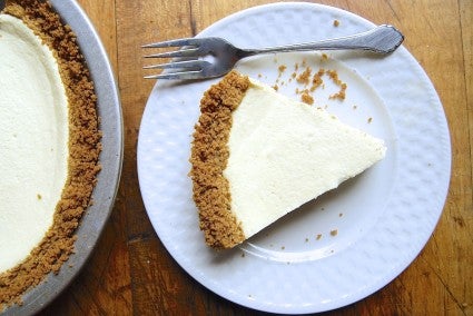 Slices of vanilla cheesecake in graham cracker crust on a white plate, with fork