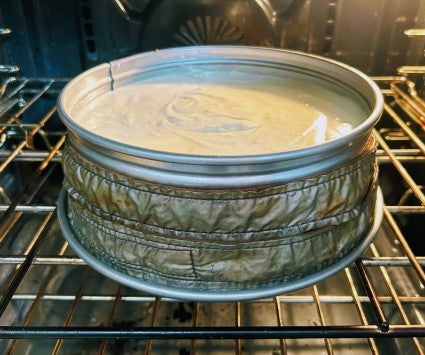 Cheesecake baking in a springform pan, the pan wrapped in cake strips