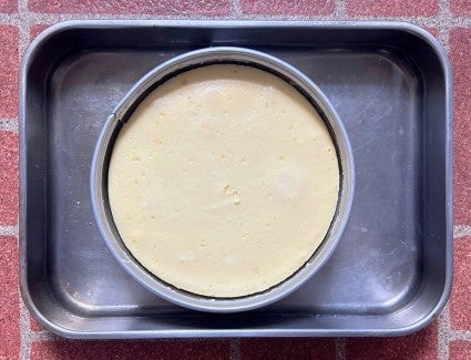 Baked cheesecake in a springform pan, the pan sitting in a larger pan of water