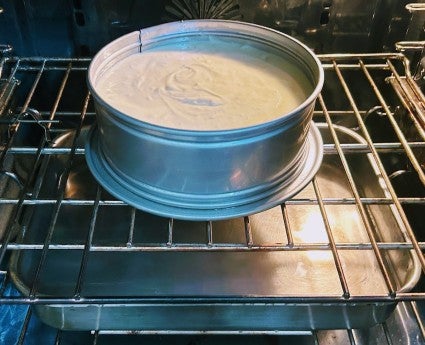 Cheesecake baking in a springform pan in the oven, set over a roasting pan to add steam to the oven. of hot water