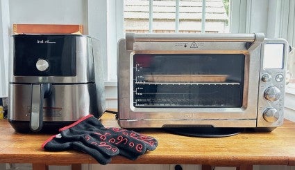 A bucket-type air fryer and toaster oven-style air fryer side by side on a wooden table.