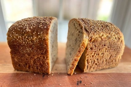 Pan loaf of multigrain sourdough bread, sliced down the center with a single cut slice resting between the two halves of the bread.