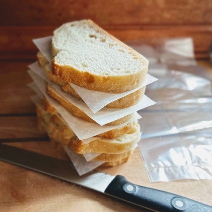 Individual slices of sourdough bread separated by pieces of parchment piled on a cutting board.