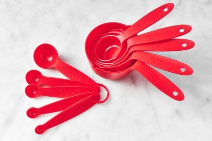 Red plastic measuring cups and spoons on marble surface