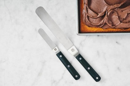 Medium and small offset spatula on a marble surface next to frosted cake