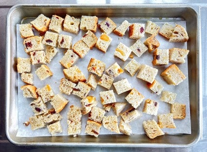 Fruited Sourdough Sandwich Bread diced into pieces and placed on a parchment-lined baking sheet to dry out.