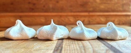 Four baked meringue kisses side by side, showing a difference in sharpness and volume.