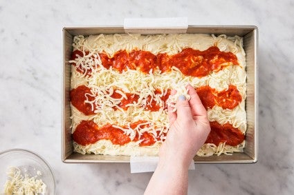 Assembling a focaccia pizza by sprinkling on cheese