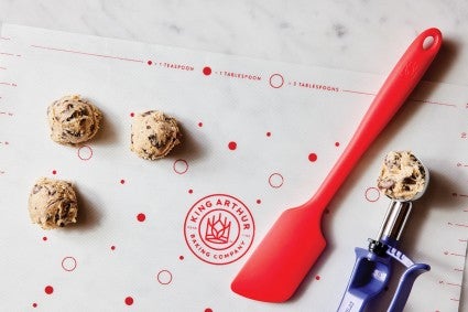 Silicone spatula next to cookie scoop and cookie dough balls on silicone baking mat